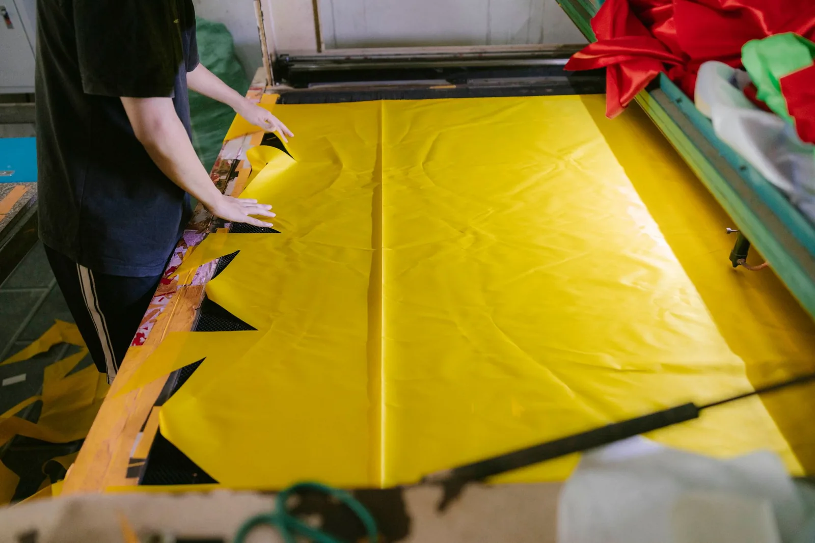 Personne étendant un grand pan de tissu jaune sur une table d'impression textile en atelier
